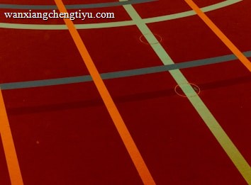 A sports court with intersecting lines in orange and blue, creating geometric patterns on a reddish-brown surface.